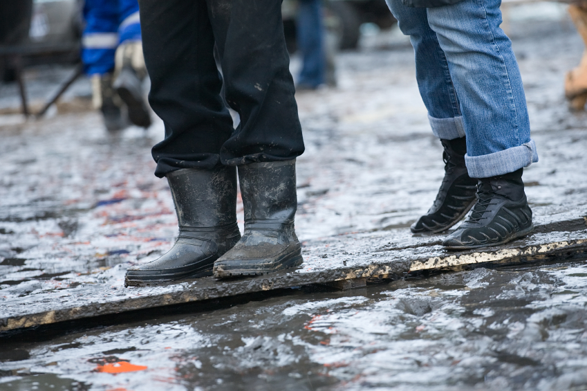 People in rubber boots and in gym shoes stand on a wooden plate in the middle of a puddle