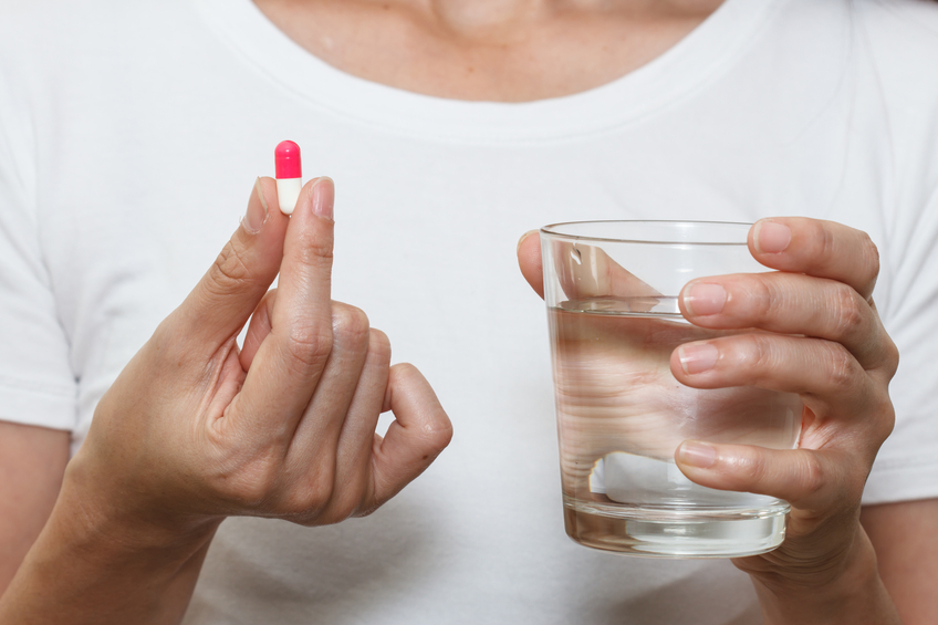 hands holding capsule pill and a glass of water